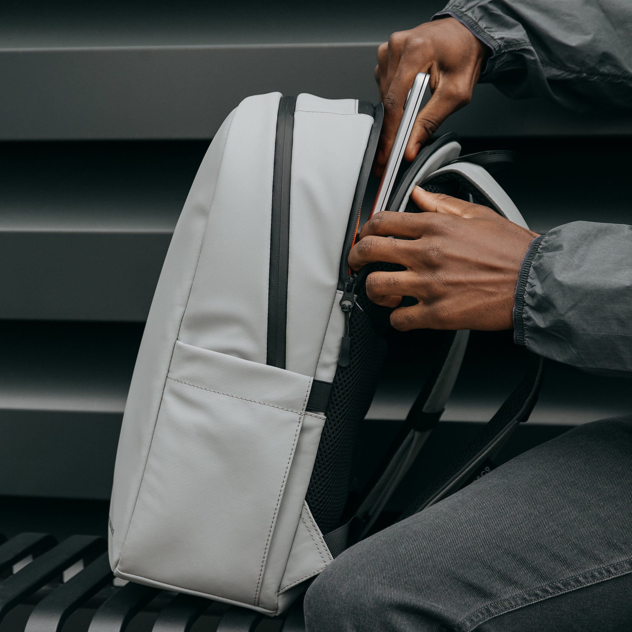 A man putting a laptop into the compartment at the back of the Everyday Backpack 20L in Concrete