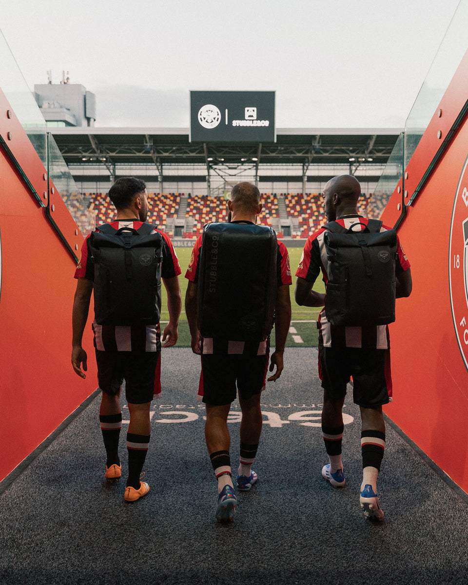 three football players walking into the stadium wearing black backpacks and rucksacks