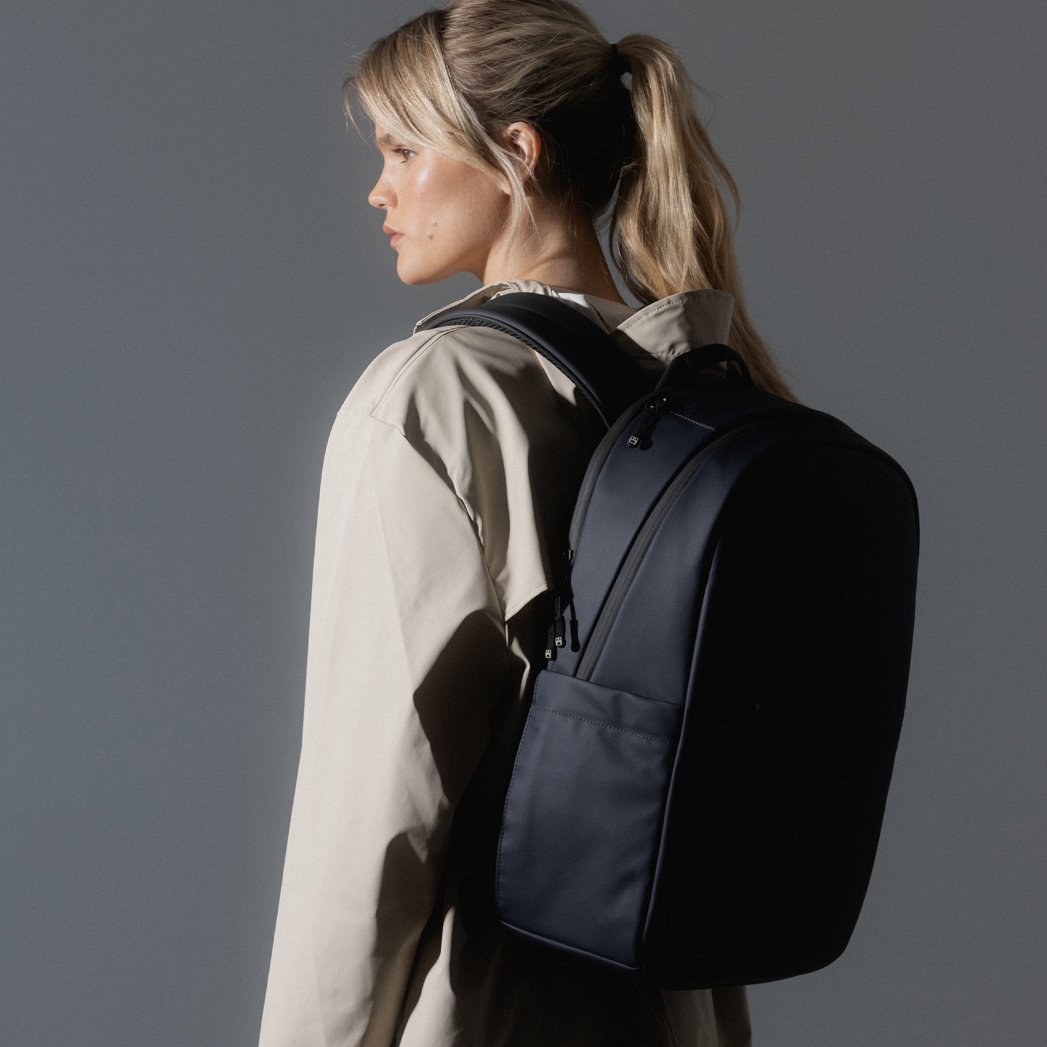 A studio shot of an Everyday Backpack 15L in Midnight Blue showing a woman wearing the bag on her back