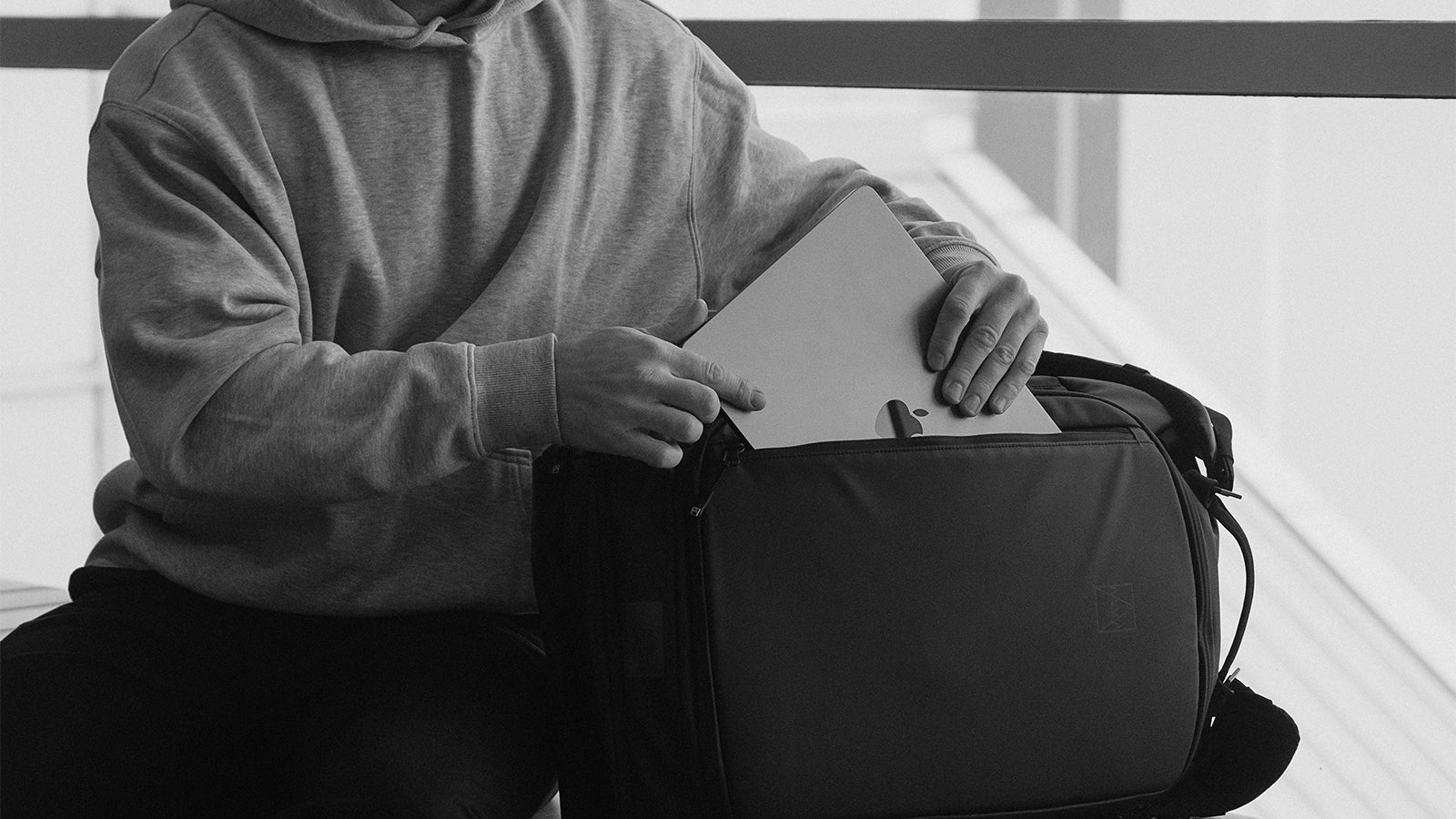 A black and white shot of a man putting a laptop into the laptop compartment in his Kit Bag 30L