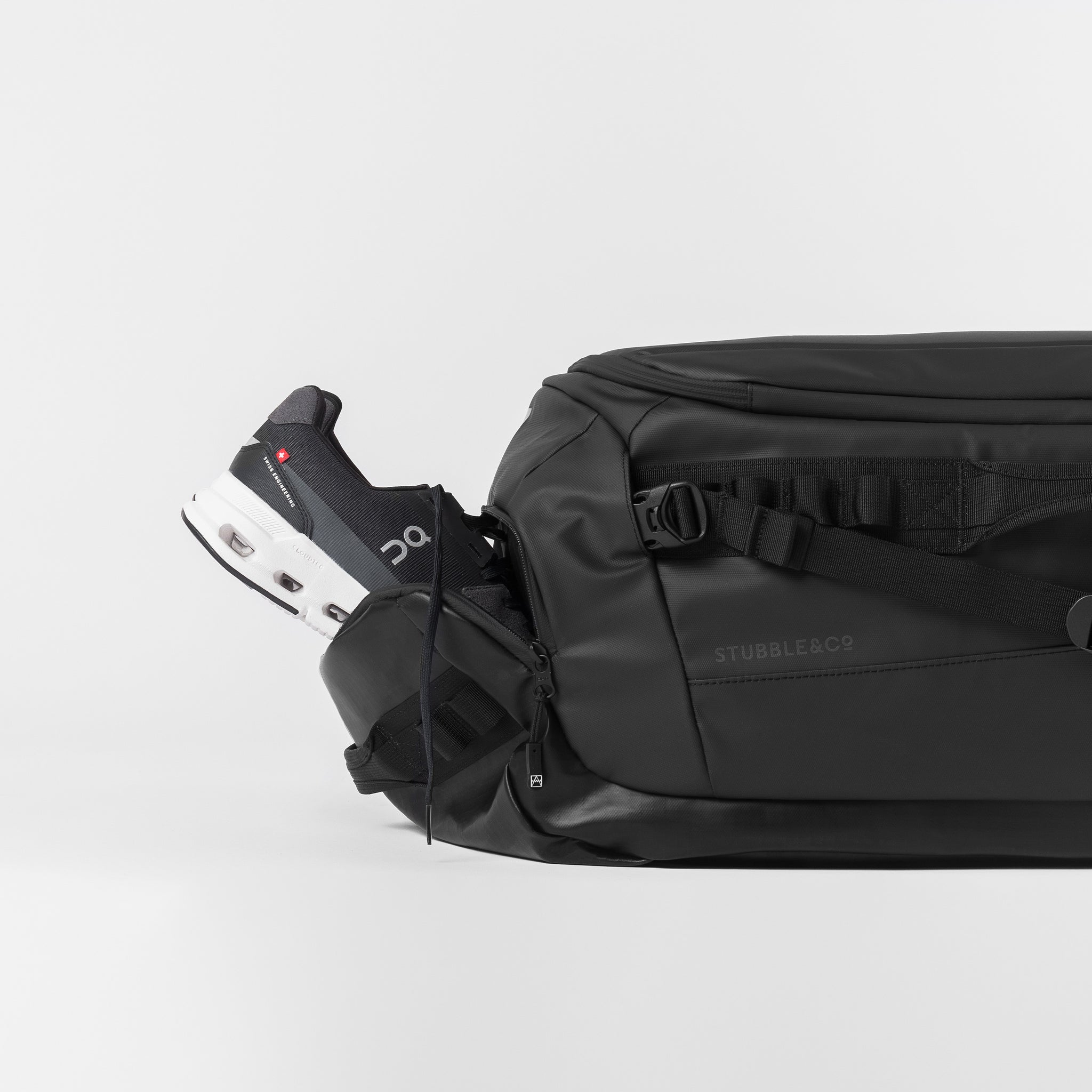 A studio shot of shoes inside the shoe compartment on the Kit Bag 65L in All Black