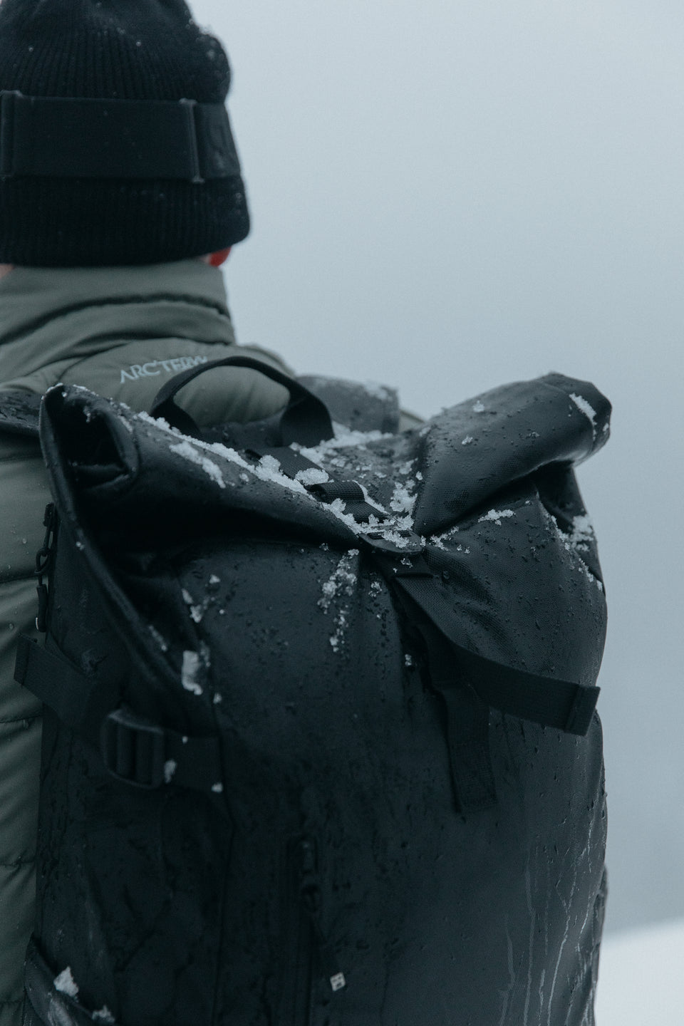 a close up of a black backpack covered in snow on a mans back 