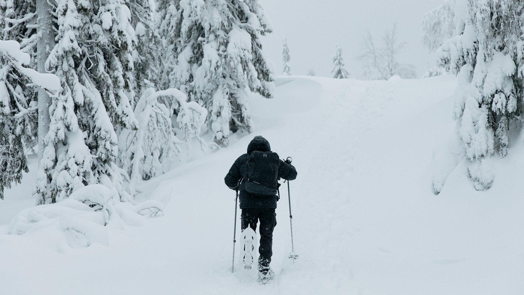 A man walking through the snow holding ski poles and wearing a black backpack