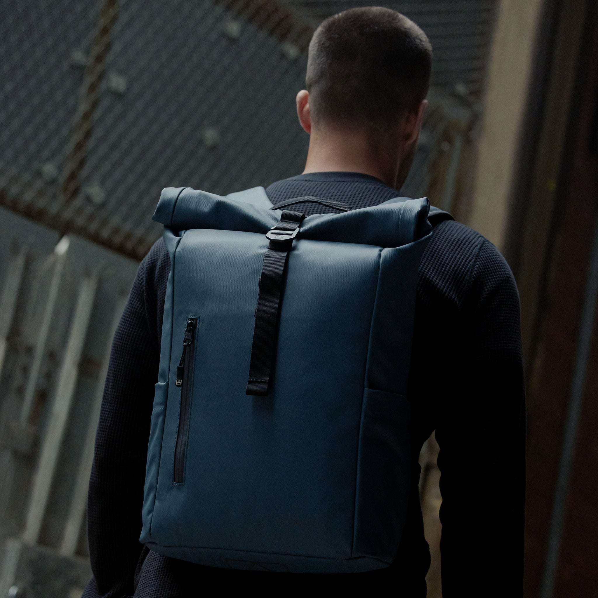 A man walking with a Roll Top 15L backpack in Tasmin Blue on his back