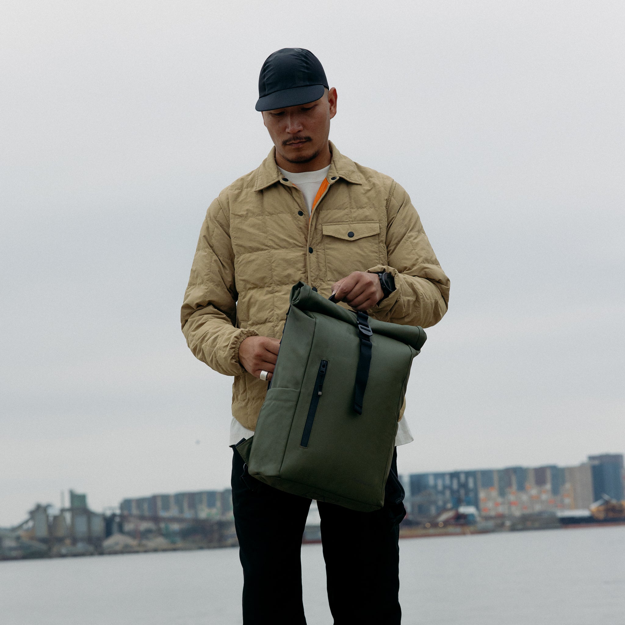 A man holding a Roll Top 15L backpack in Urban Green