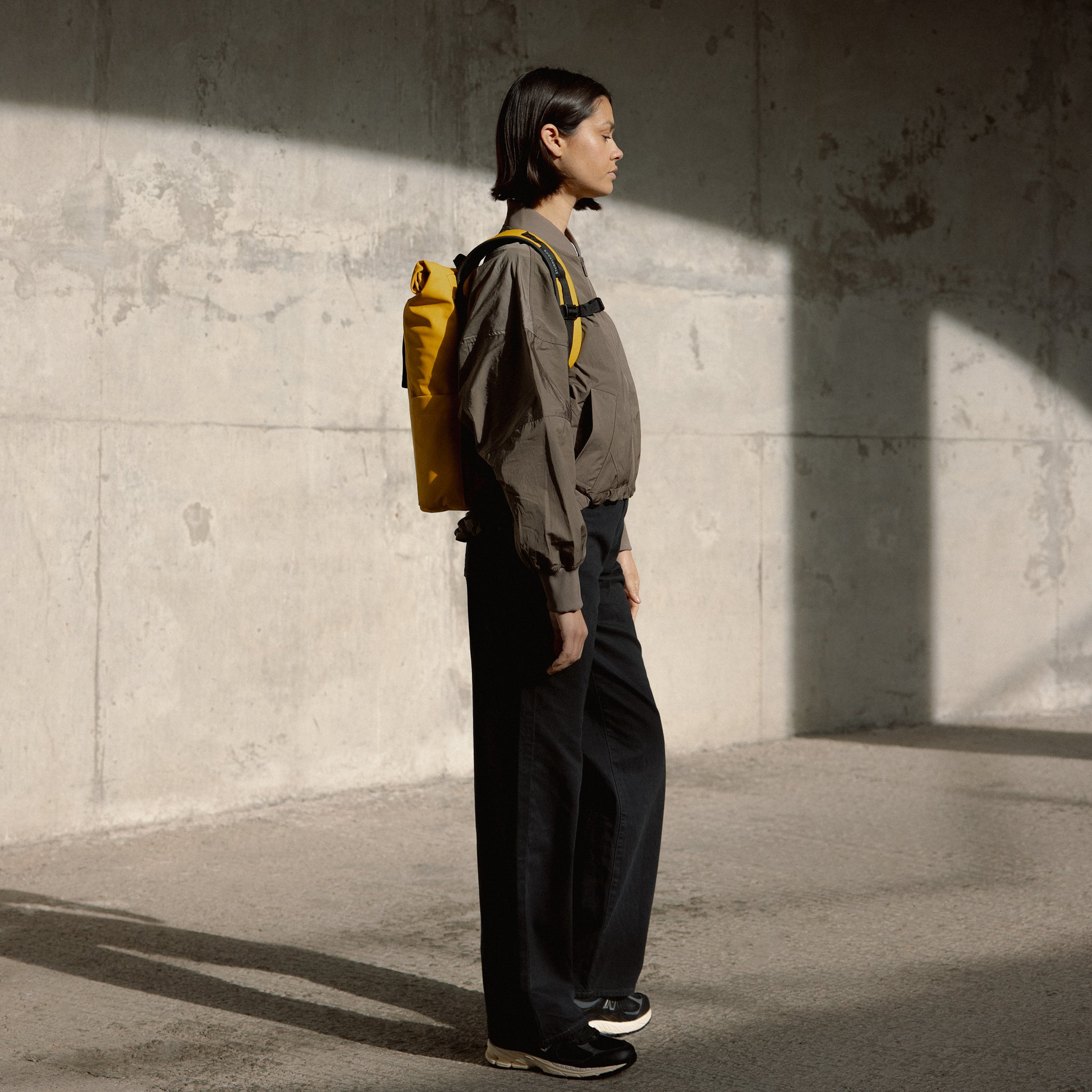 a woman facing the side wearing a Yellow roll top 15l on her back