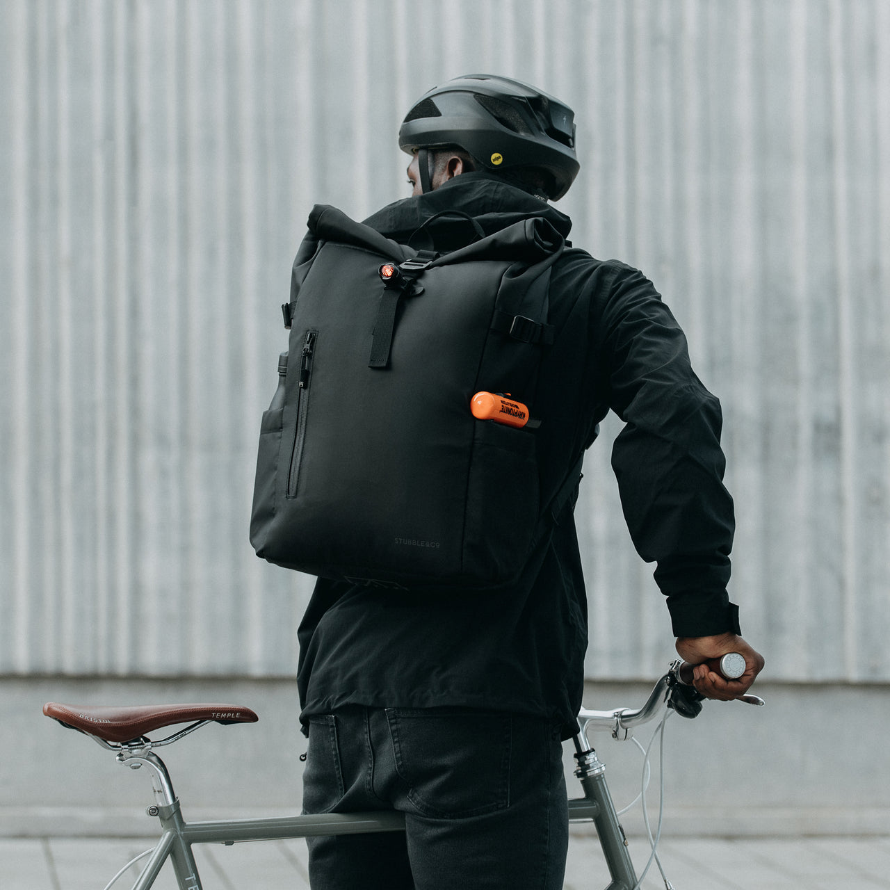 Man wearing The Roll Top 20L Backpack in All Black on a bike