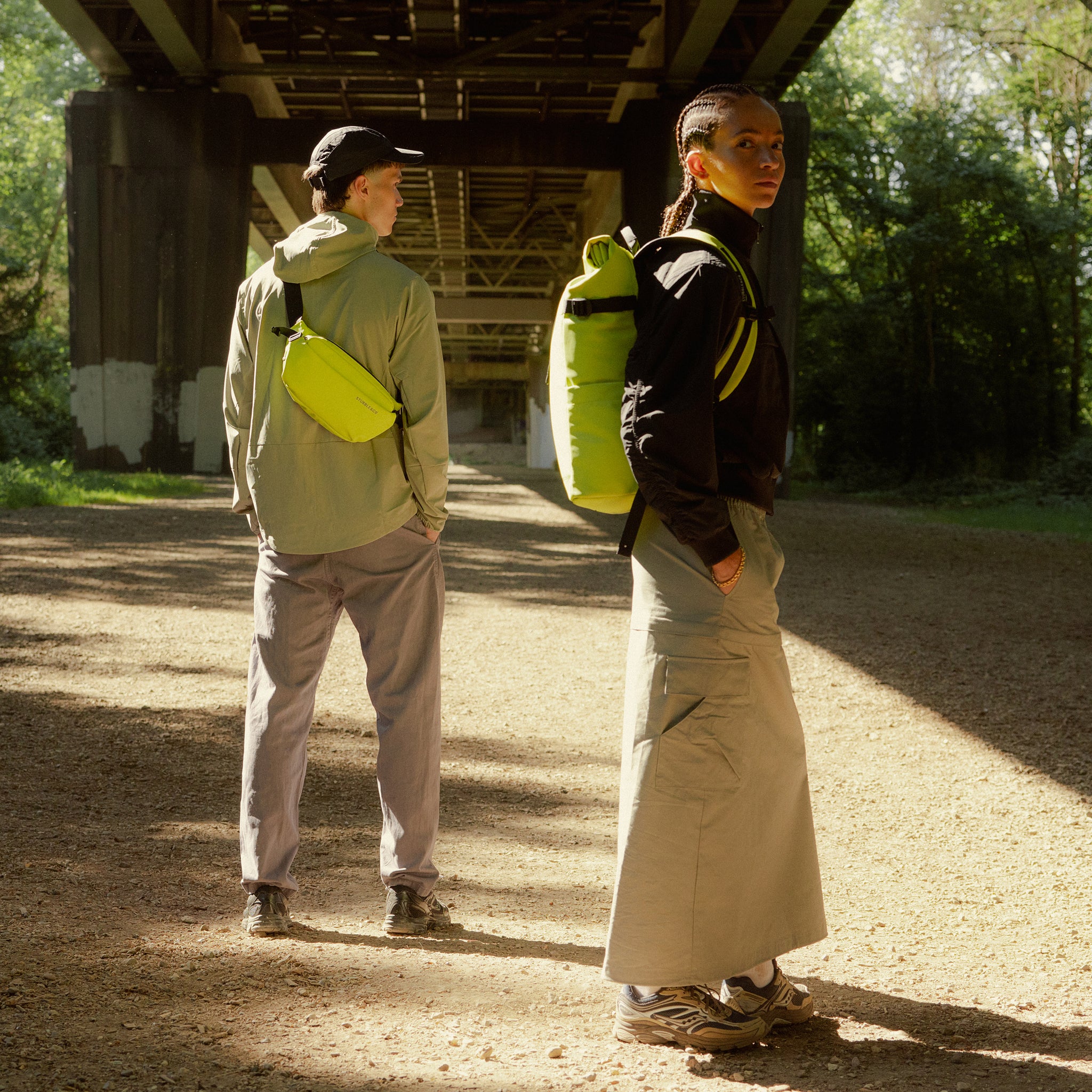 A woman wearing a Roll Top 20L on her back and a man wearing a Crossbody on his back in Volt