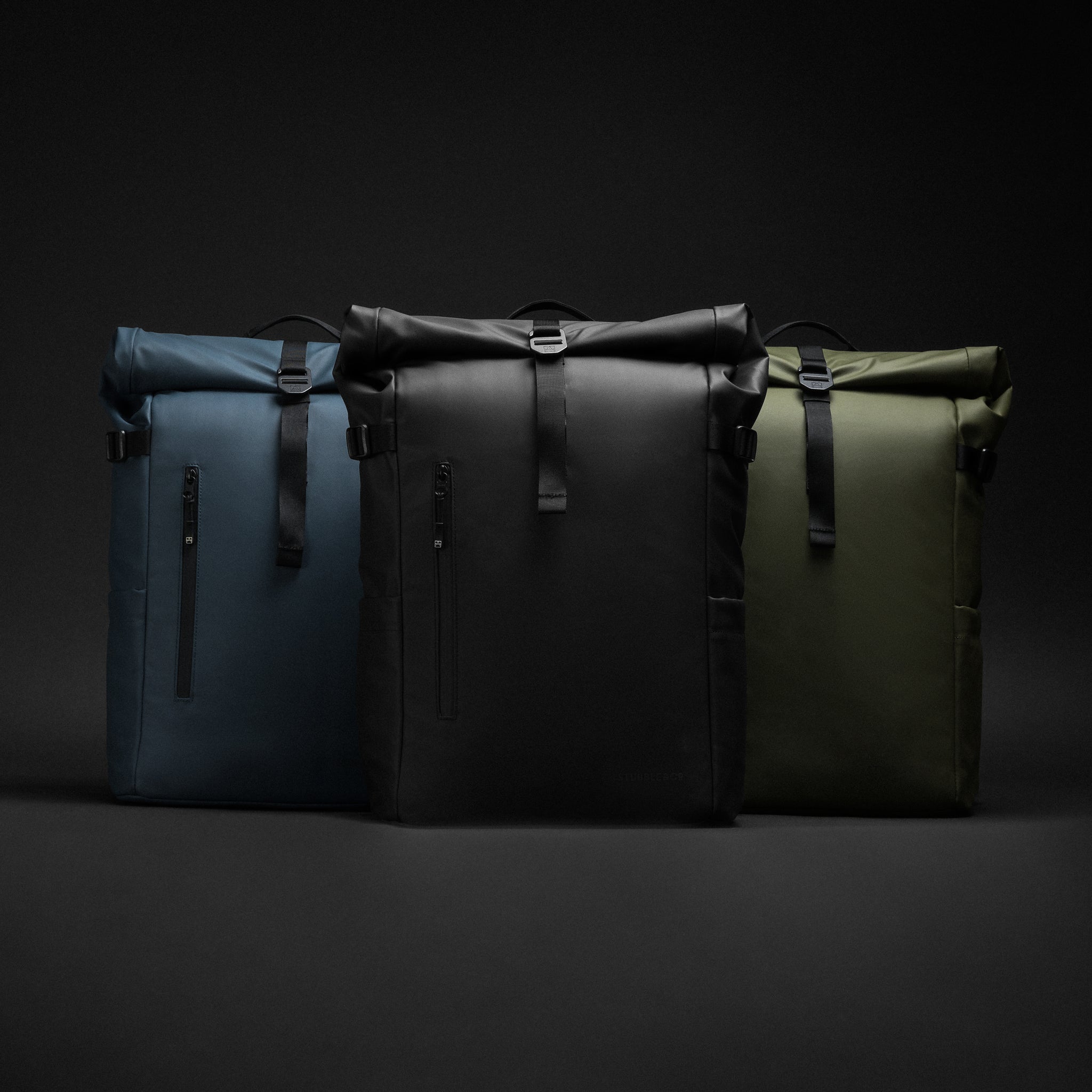 A picture of the Roll Top 30L backpacks in a studio in all 3 colours, Black, blue and Urban Green