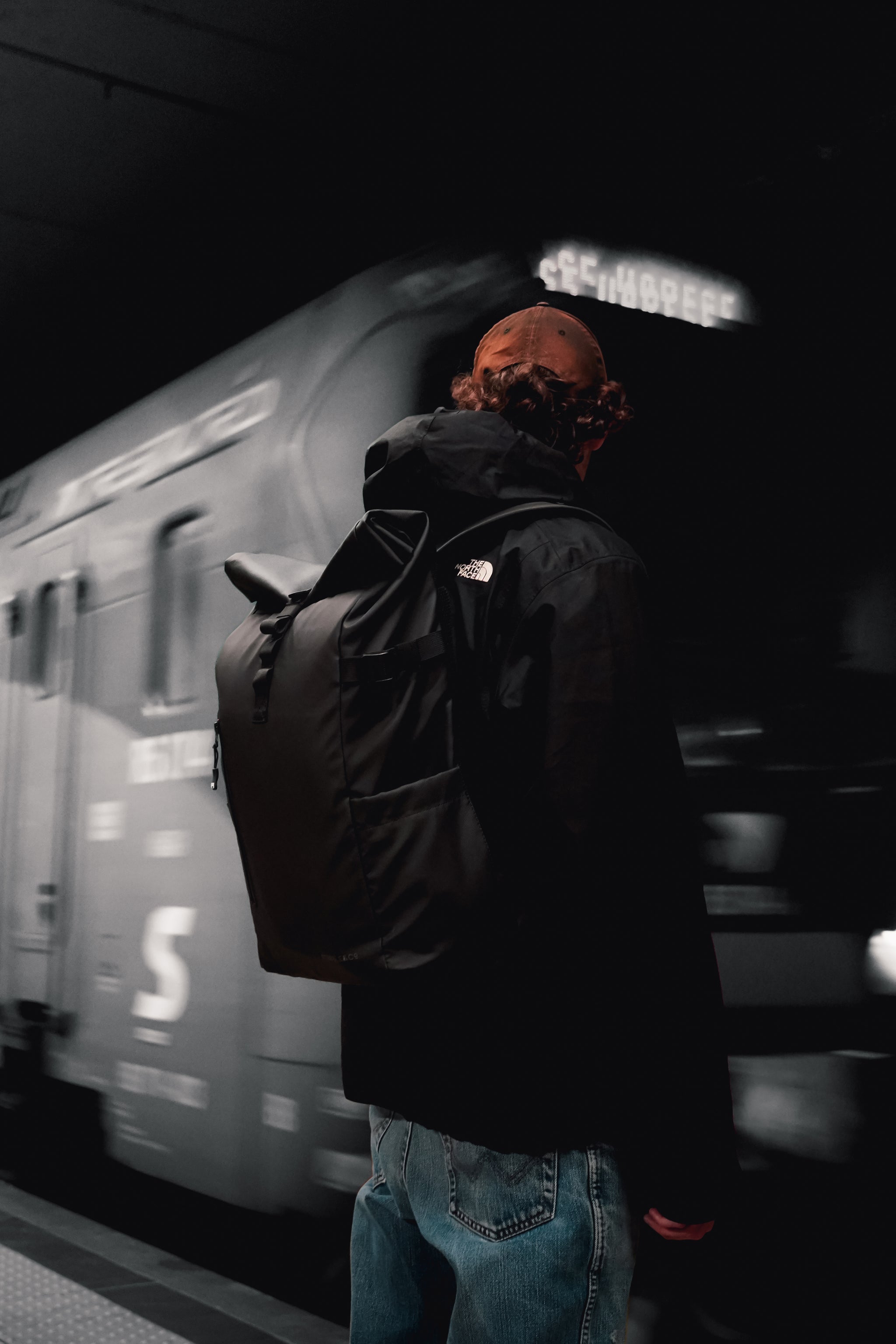 Man wearing a black Roll Top backpack by a train that is moving