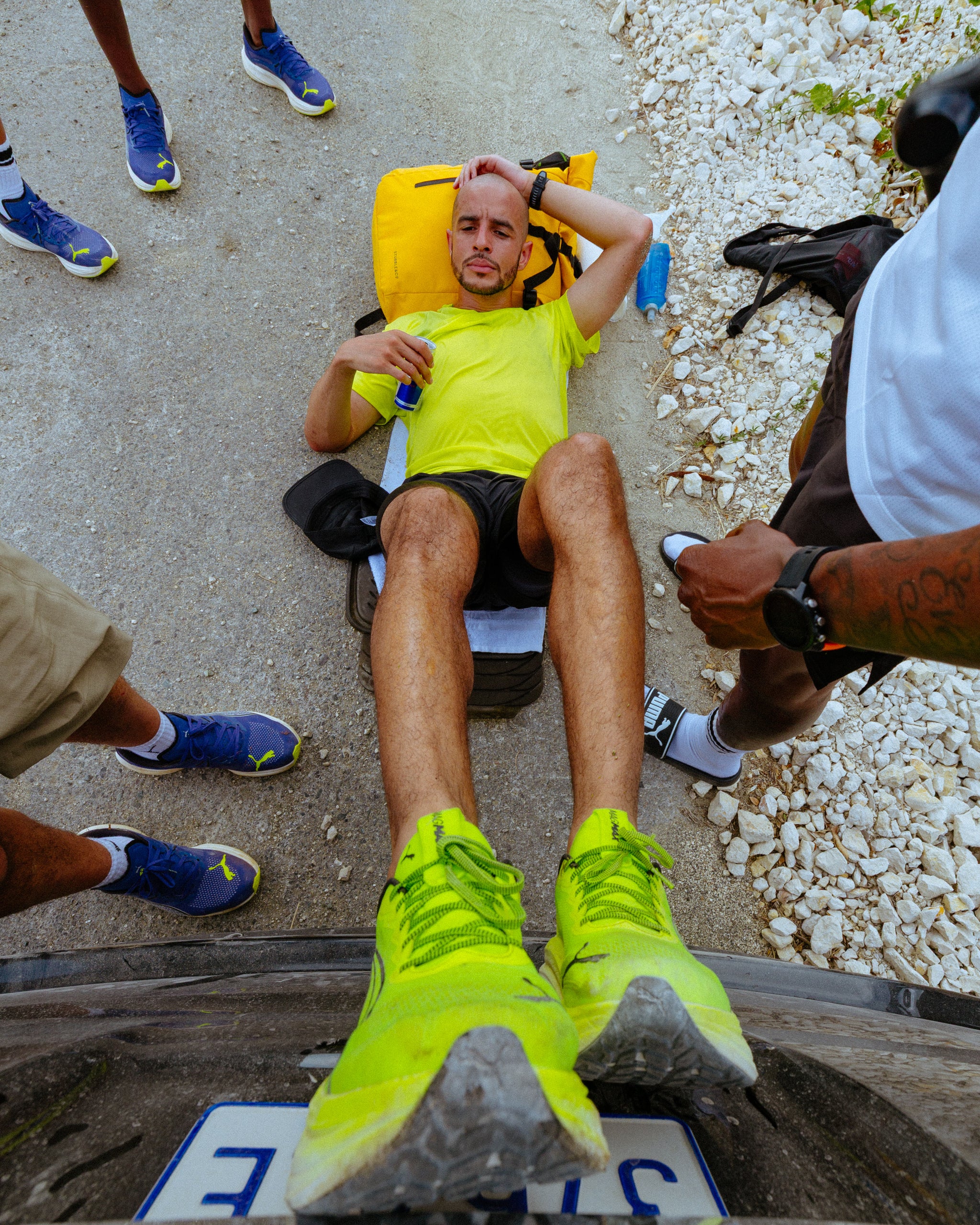 A man with his feet against a wall whilst lying on the pavement with a Roll Top in yellow as a pillow