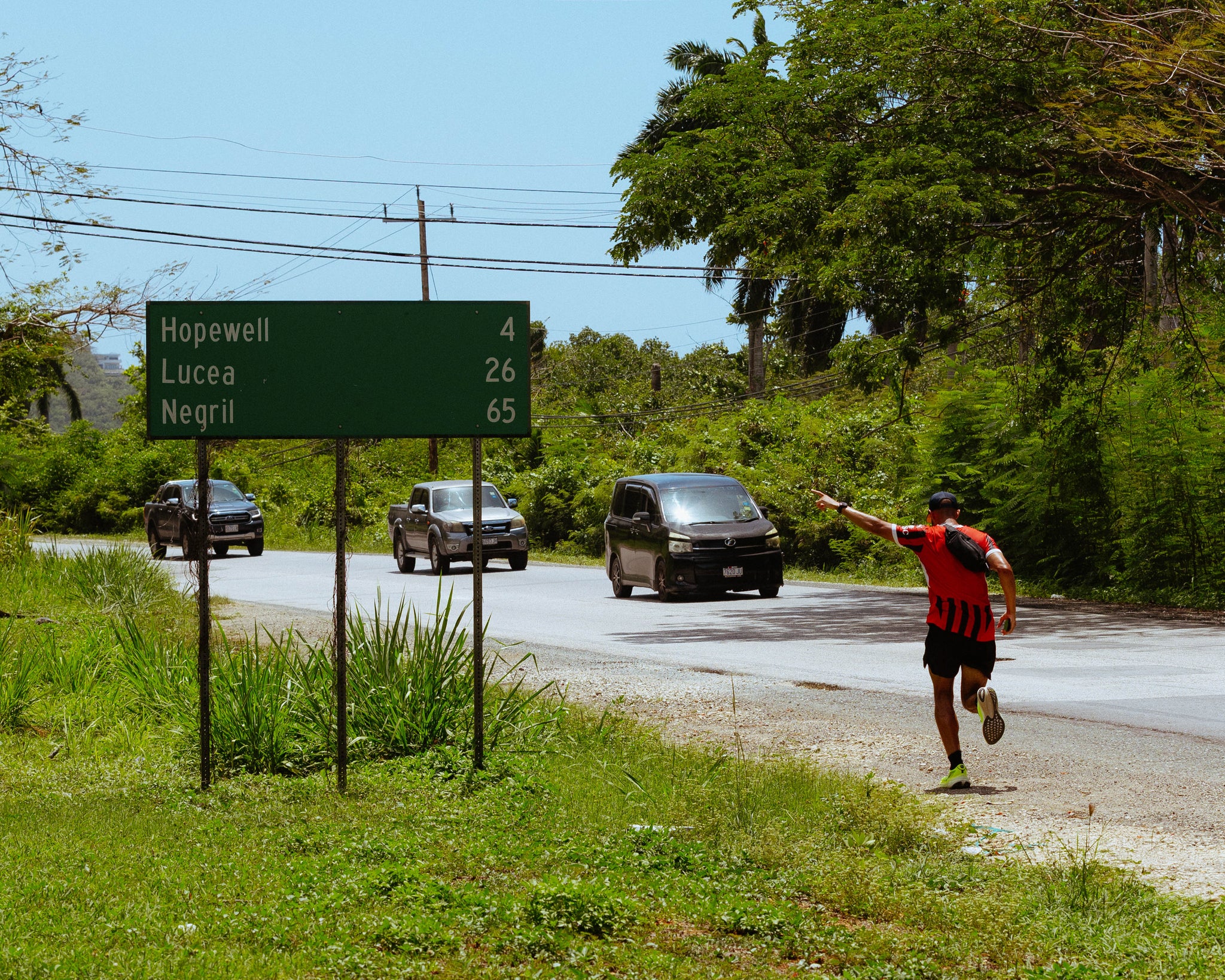 A man running down the street whilst pointing at the road sign during his challenge to run across Jamaica
