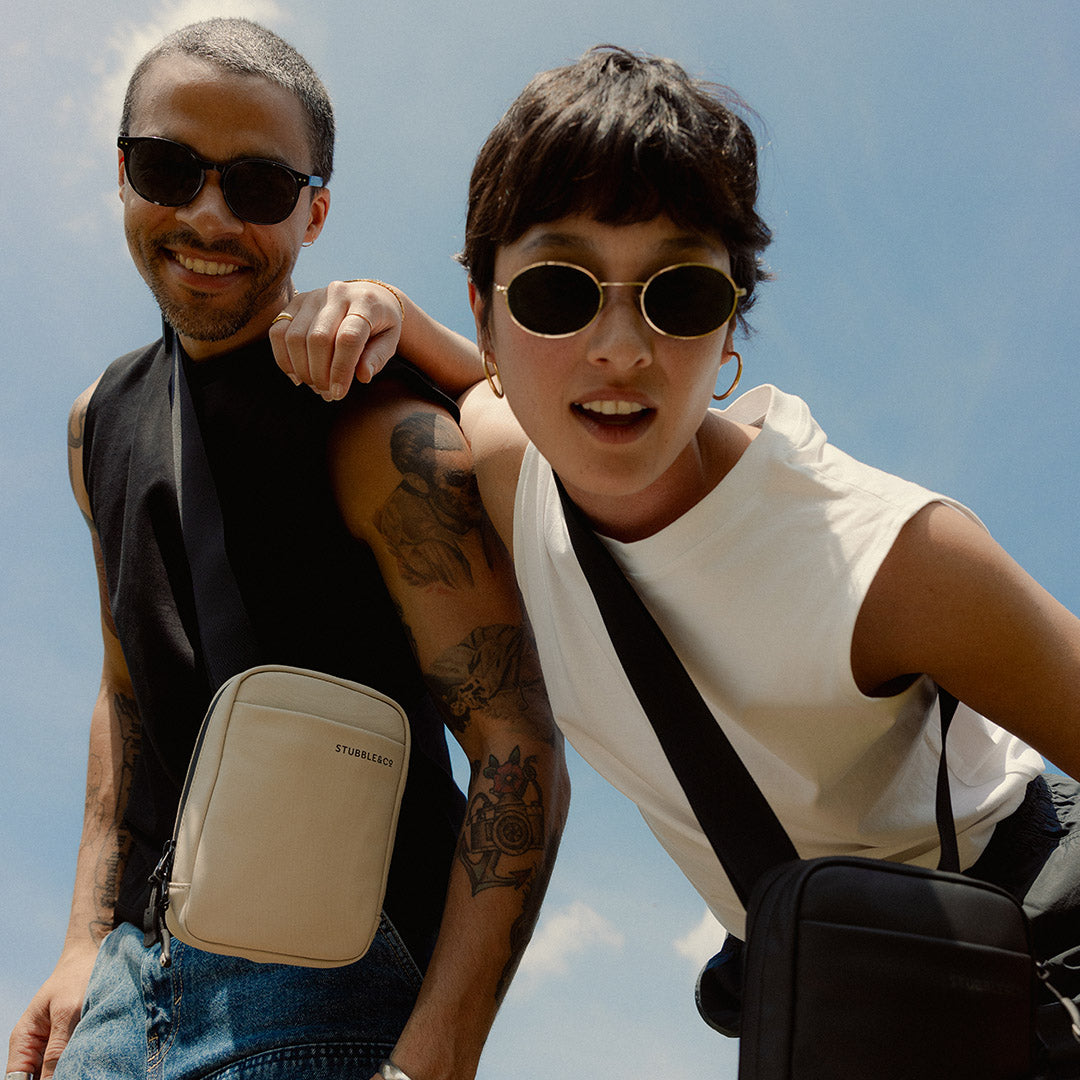 a mand an woman looking down towards the camera wearing an all black and Sand shoulder bag