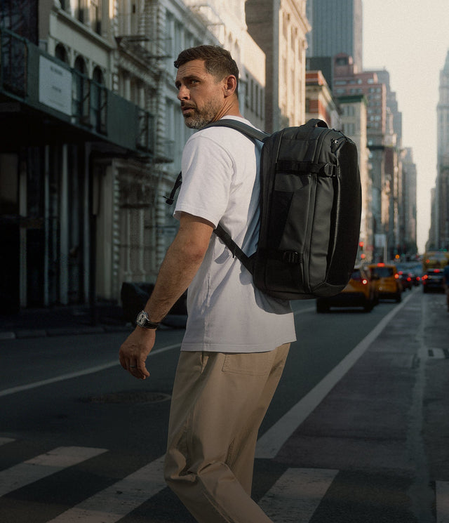 A man standing on the pavement in New York wearing a Hybrid Backpack 30L in Black on his back-mobile