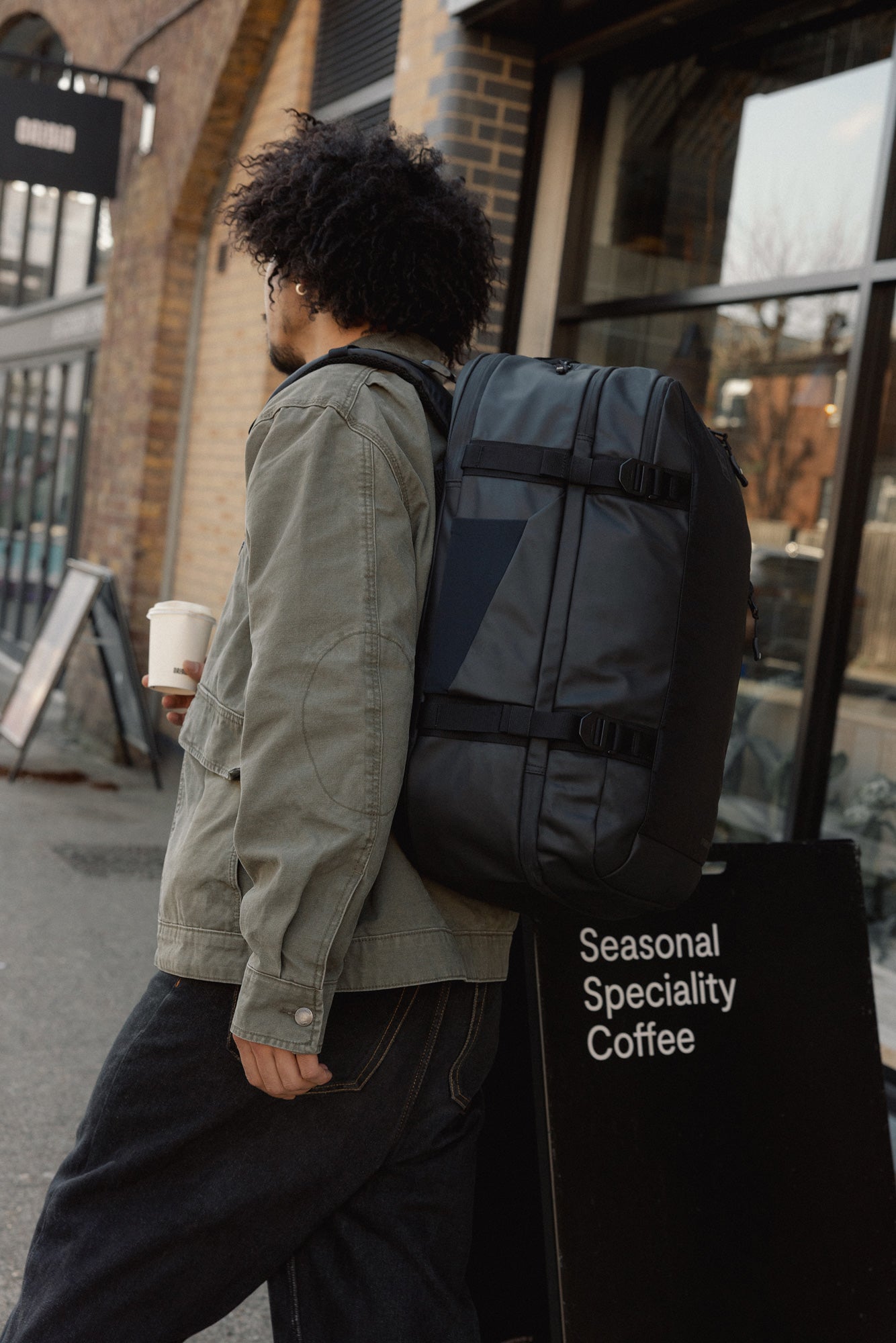 Person with a backpack walking past a coffee.