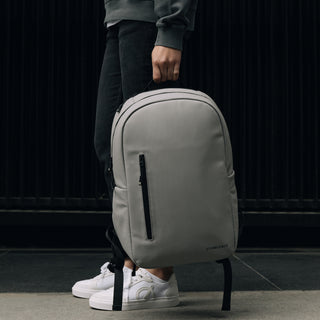 Person carrying grey backpack by handle on top