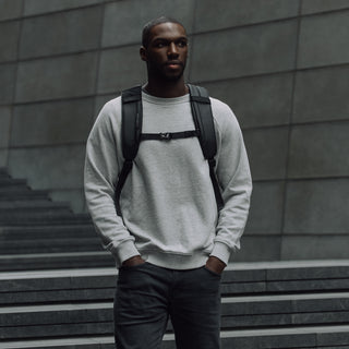 Man in grey jumper wearing backpack standing on steps