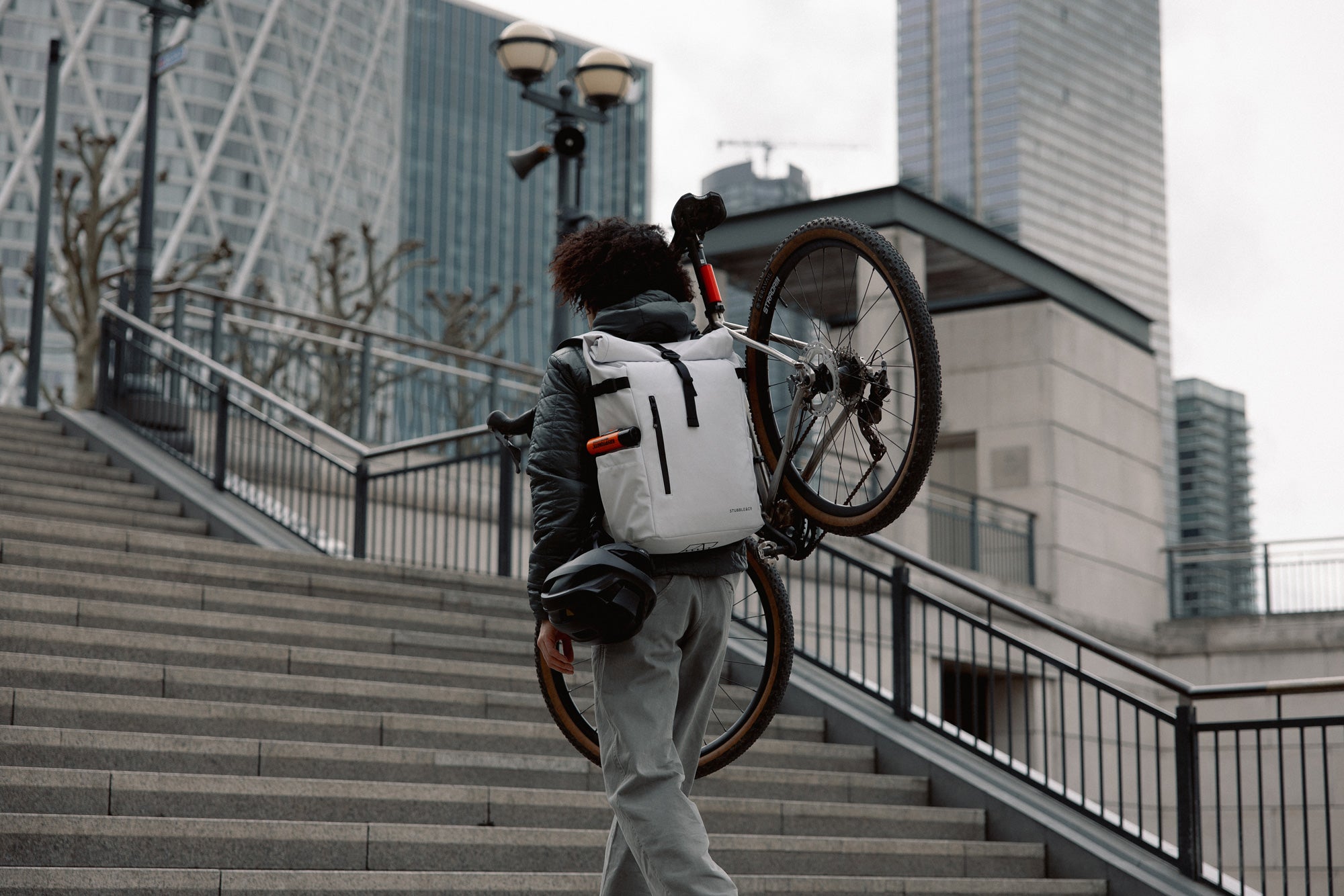 Person carrying a bicycle on a city staircase with buildings in the background