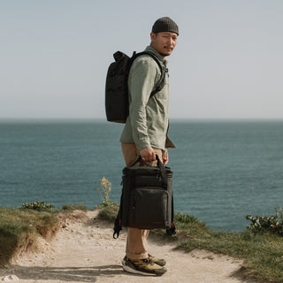 Man wearing black backpack and holding cooler bag standing by the sea