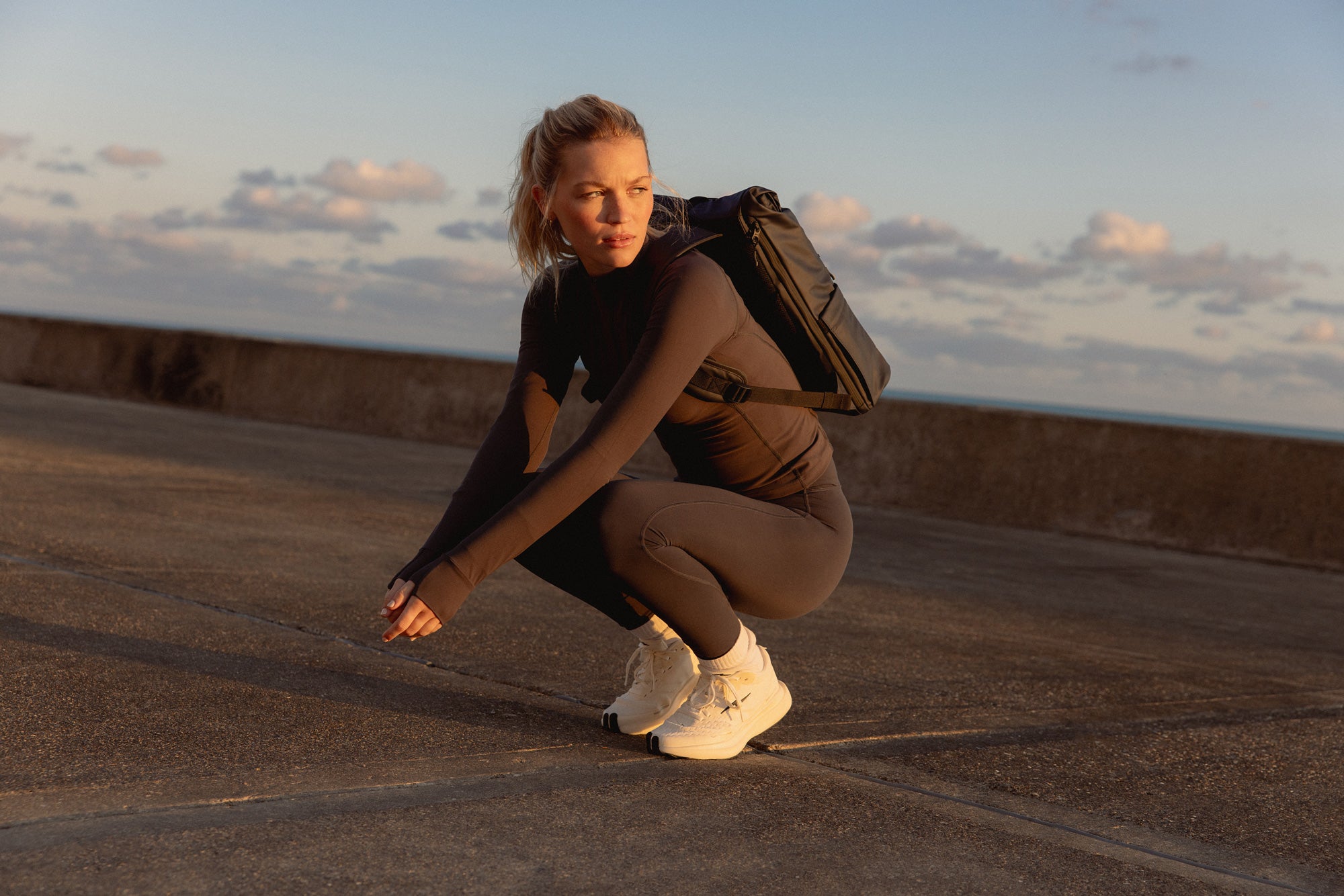 Woman with a backpack crouching with a cloudy sky background