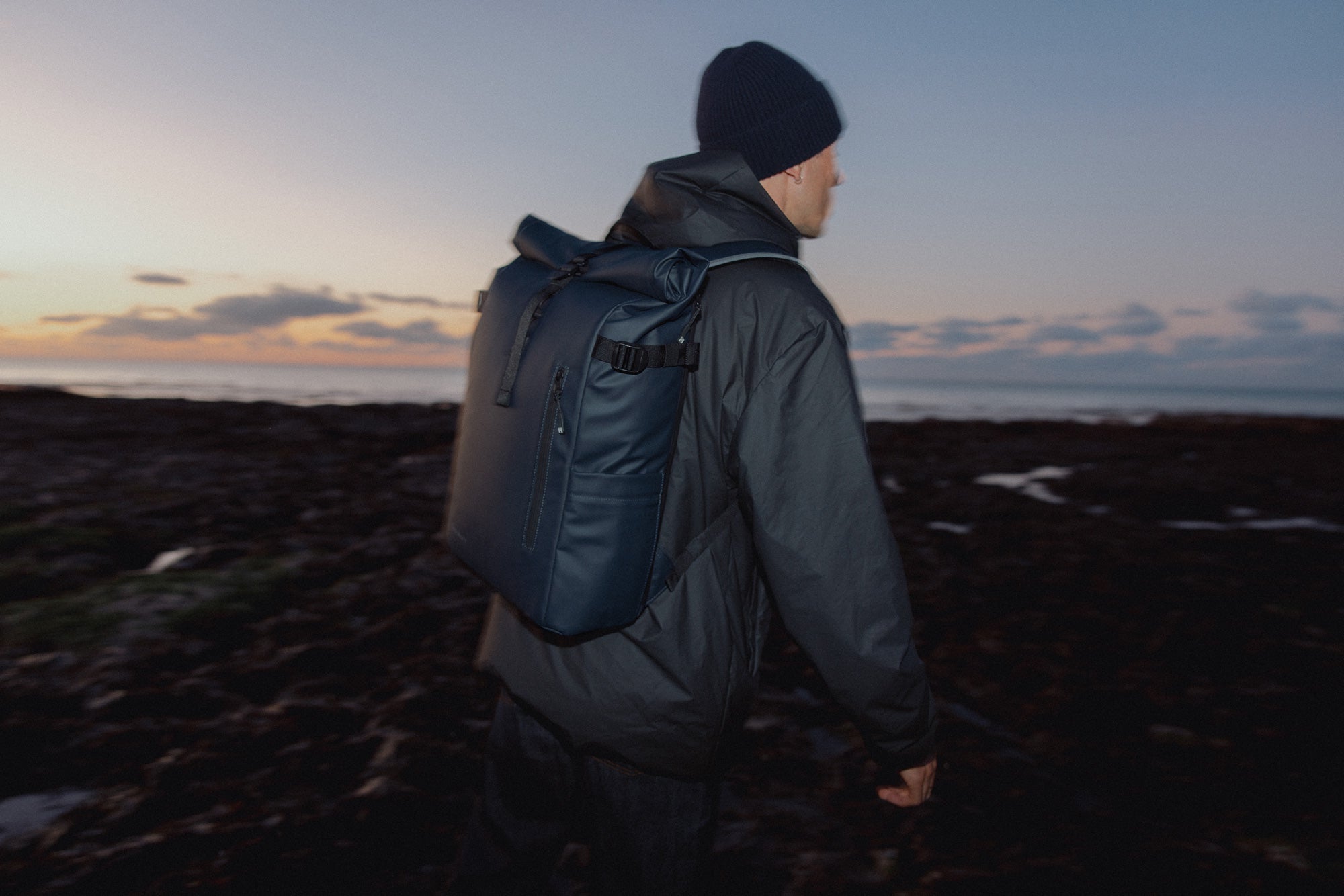Person wearing a jacket with a backpack on the beach at sunset
