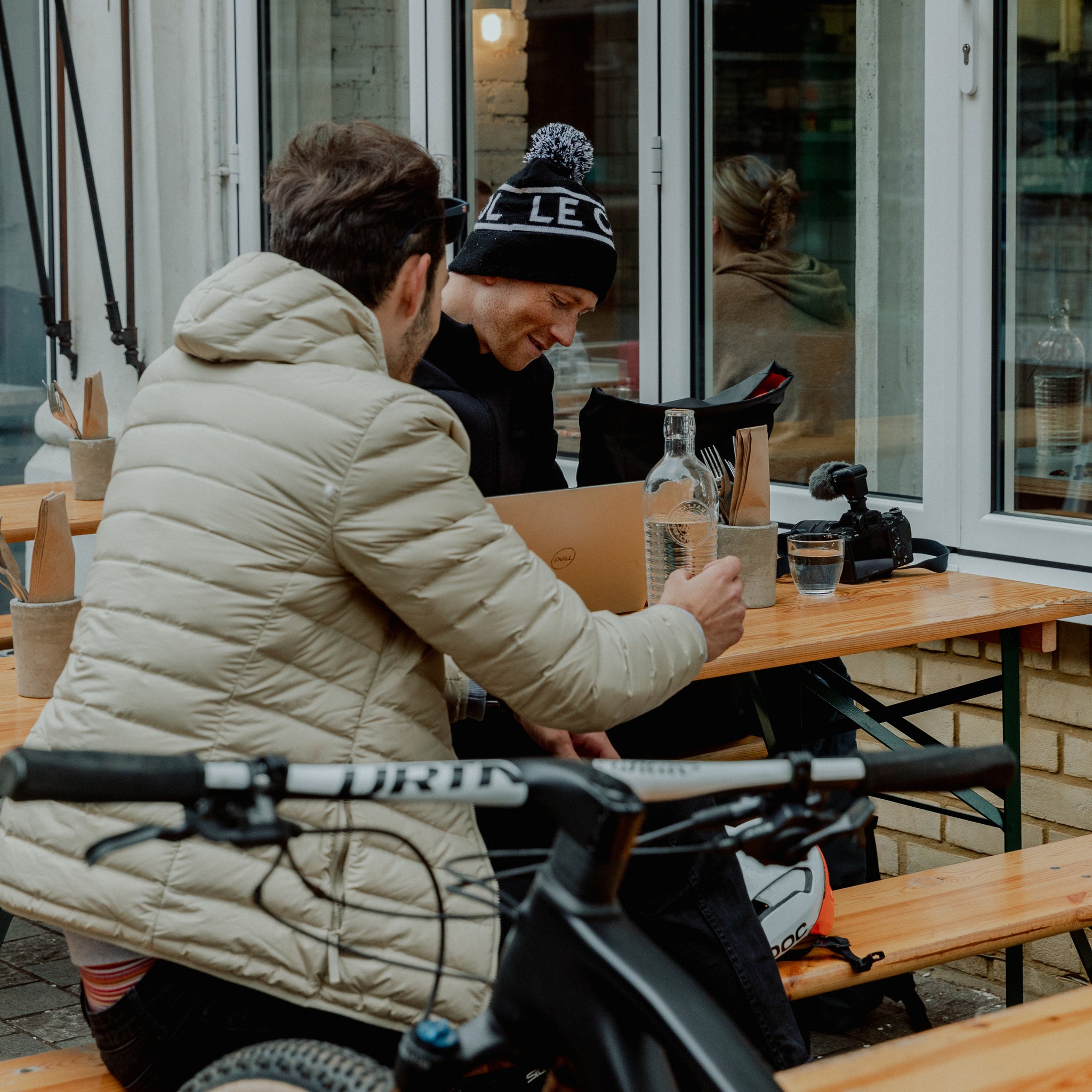 2 men sitting outside a cafe on a bench