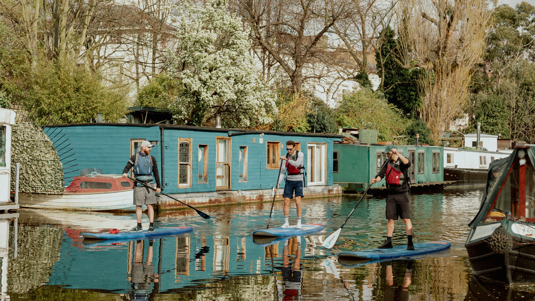 3 men paddle boarding up a river in the sun