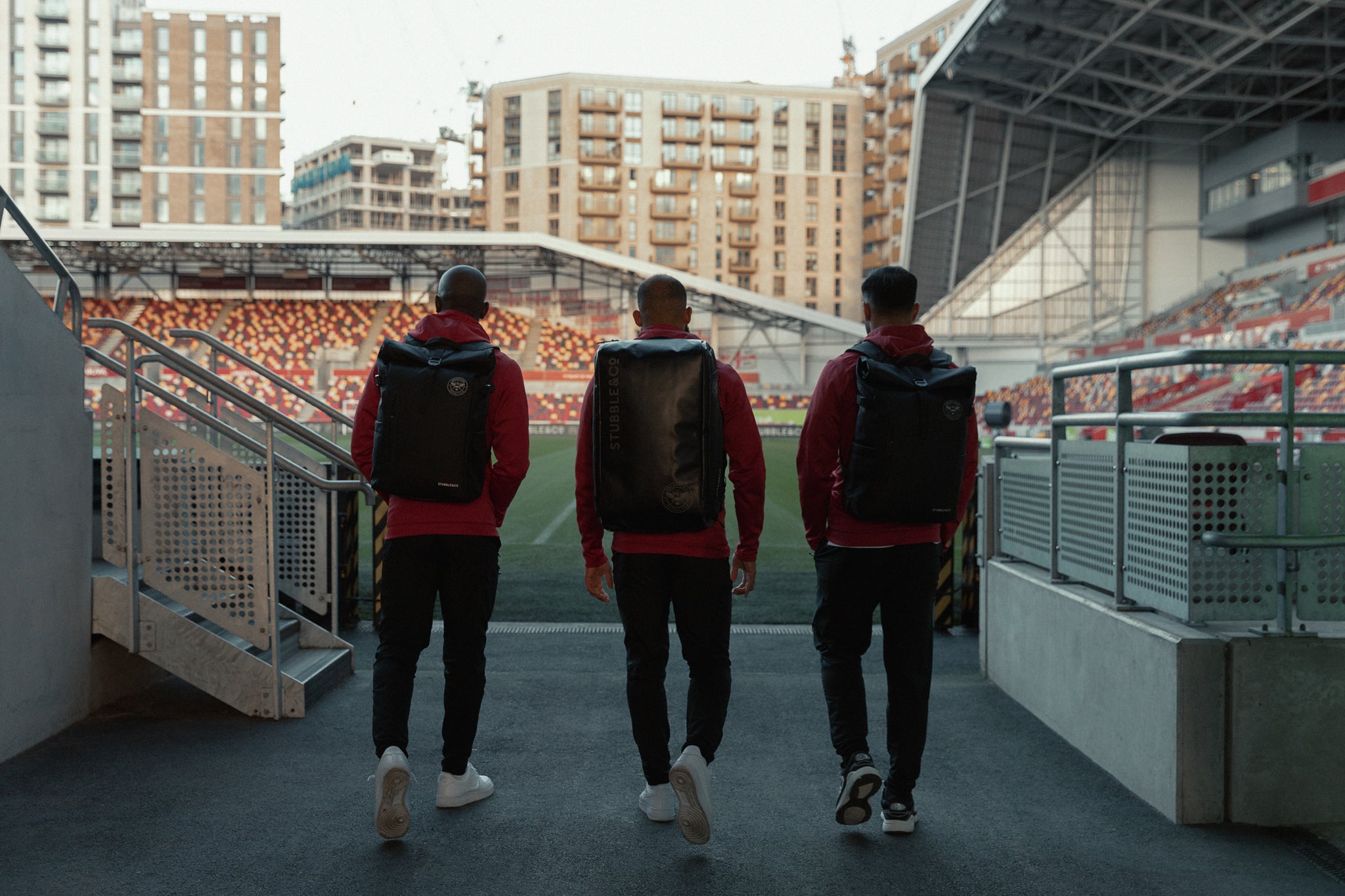 three football players walking towards the pitch wearing black backpacks and rucksacks