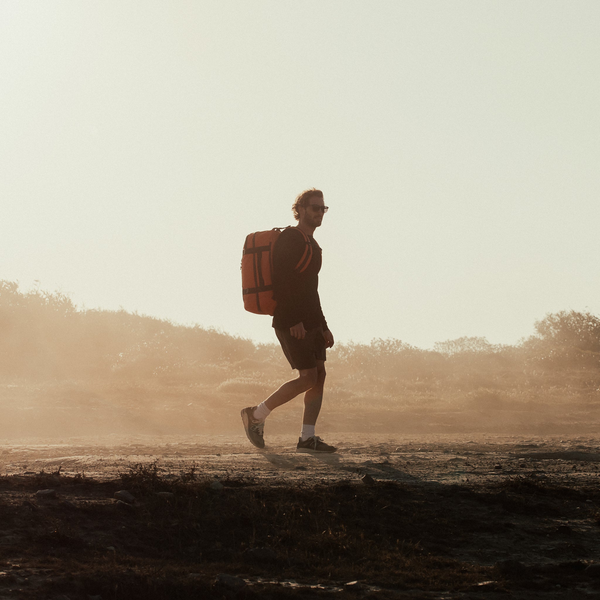 A man walking with an Adventure Bag in Ember Orange, shot from the side.