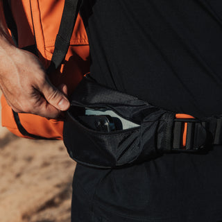 Close up of the waist strap on the Ember Orange Adventure Bag. A phone is being zipped into this.