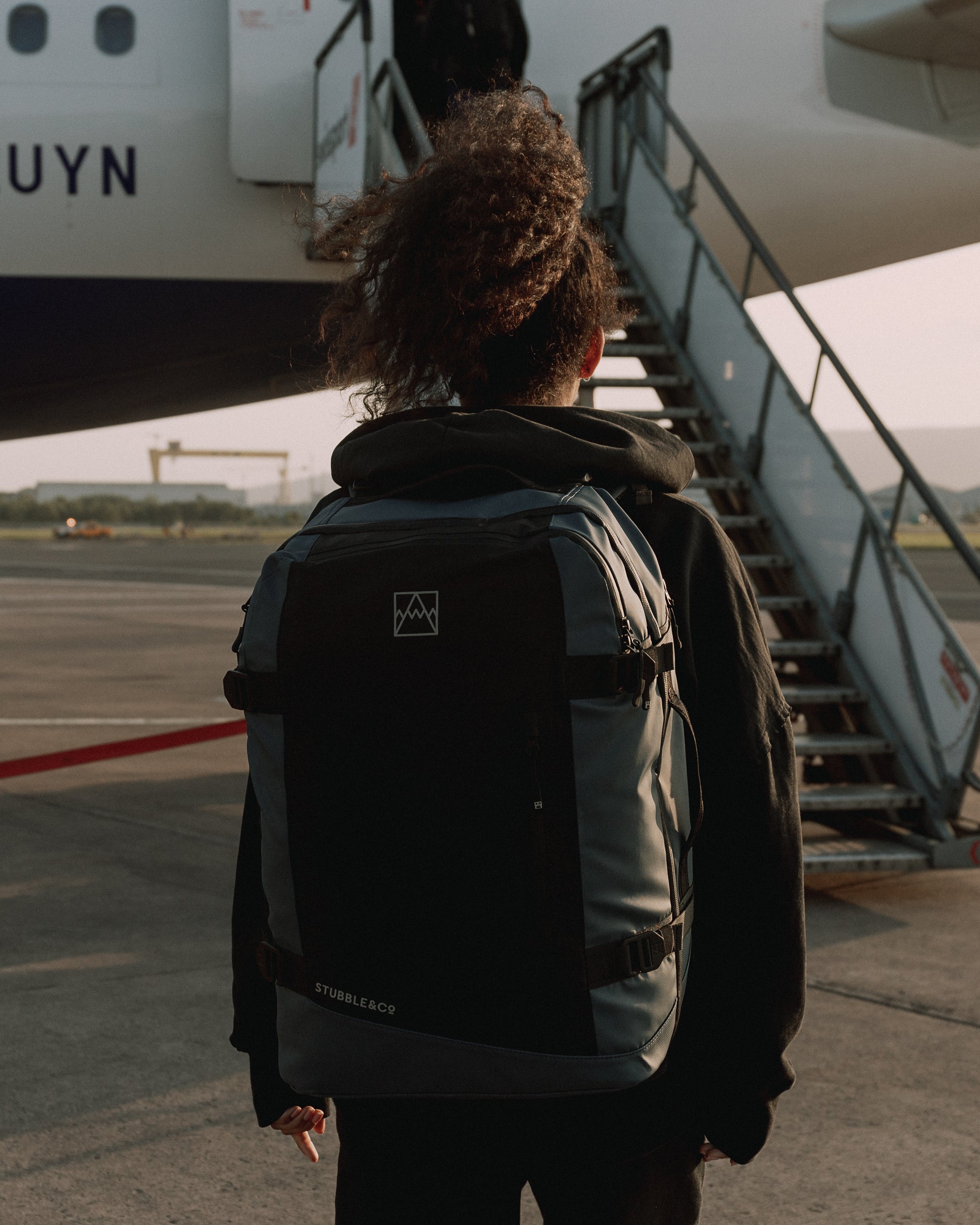 Back of a women walking onto a plane wearing a large Tasmin Blue adventure travel backpack