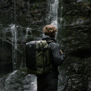 A man wearing the Urban Green Adventure Bag while looking at a waterfall. Shot from the back.