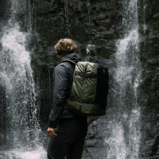 A man wearing the Urban Green Adventure Bag while looking at a waterfall. Shot from the side.