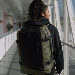 Female model walking through a corridor while wearing The Adventure Bag Urban Green in Shot from the back.