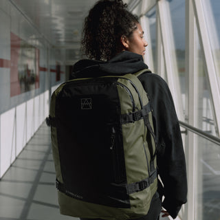 Female model walking through a corridor while wearing The Adventure Bag in Urban Green. Shot from the back.