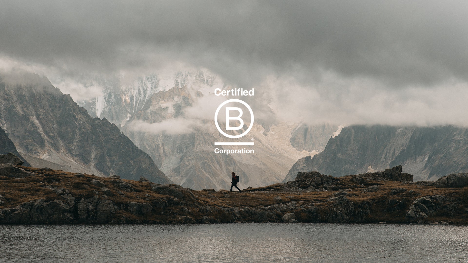 A photo of a man walking in front of a mountain range with the B Corporation logo in the middle of the image
