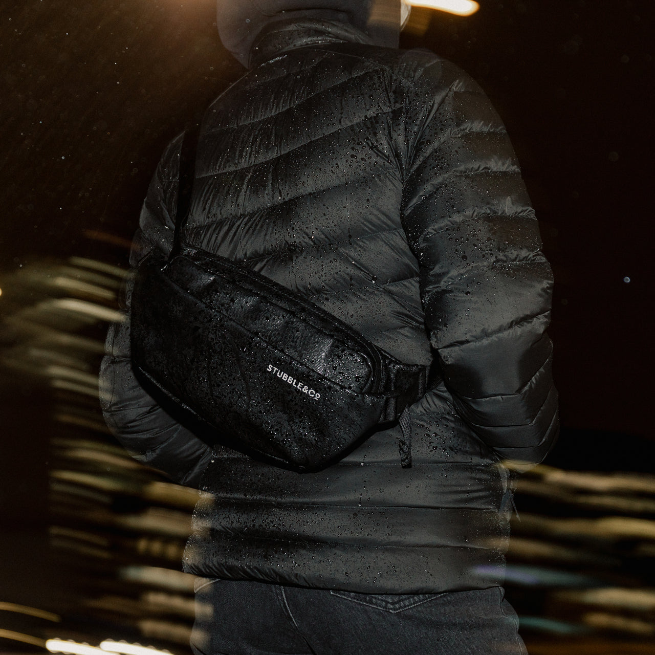 A close up of the All Black Crossbody on a woman's back in the rain showing the wateproof material