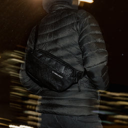 A close up of the All Black Crossbody on a woman's back in the rain showing the wateproof material