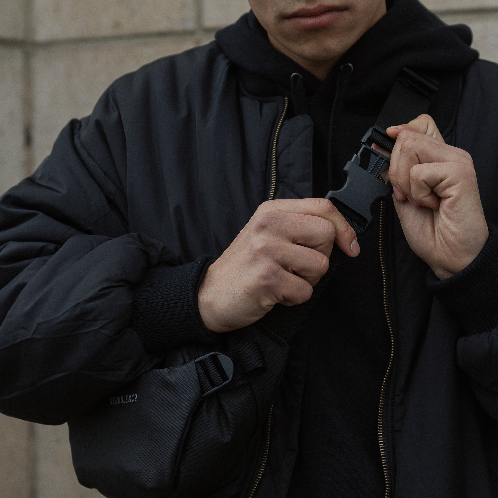 A man fastening the clip on the strap of an All Black crossbody bag