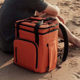 Side andle view of The Cooler in Ember Orange on the beach with a man sat next to it.