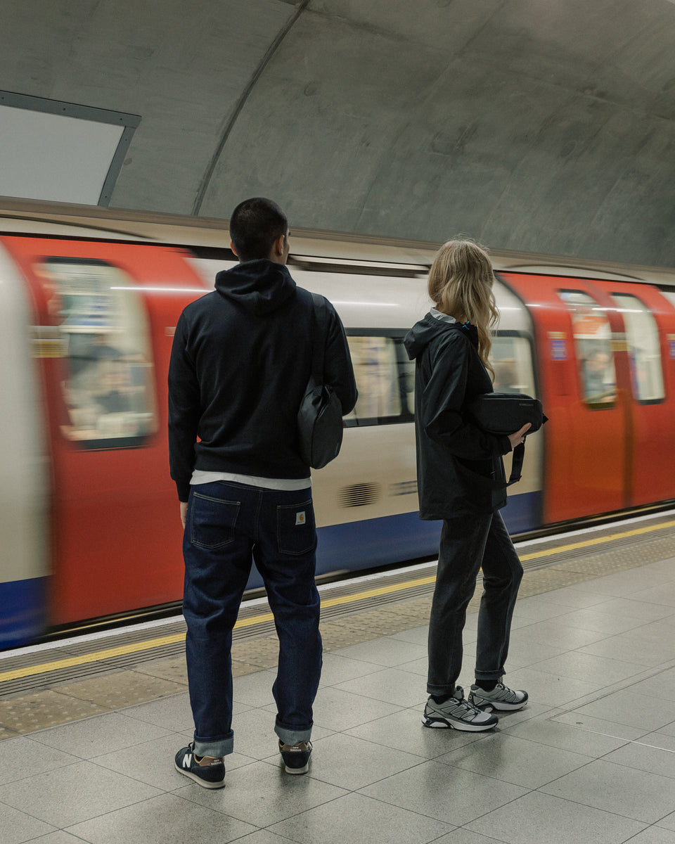Man and women by underground tube train with black crossbody bags