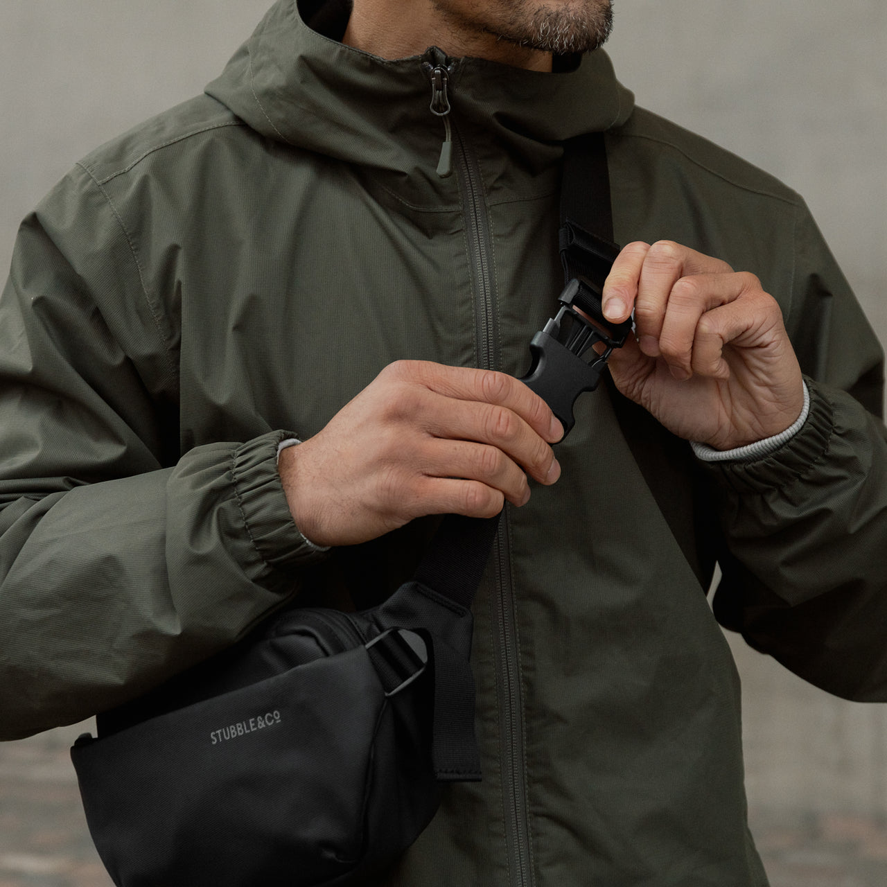 A man wearing an All Black Crossbody bag and he is doing up the clip on the adjustable strap