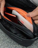 an interior shot of the All Black Crossbody bag showing the orange lining of the bags and the items inside the bag which are a card holder, a book and an umbrella