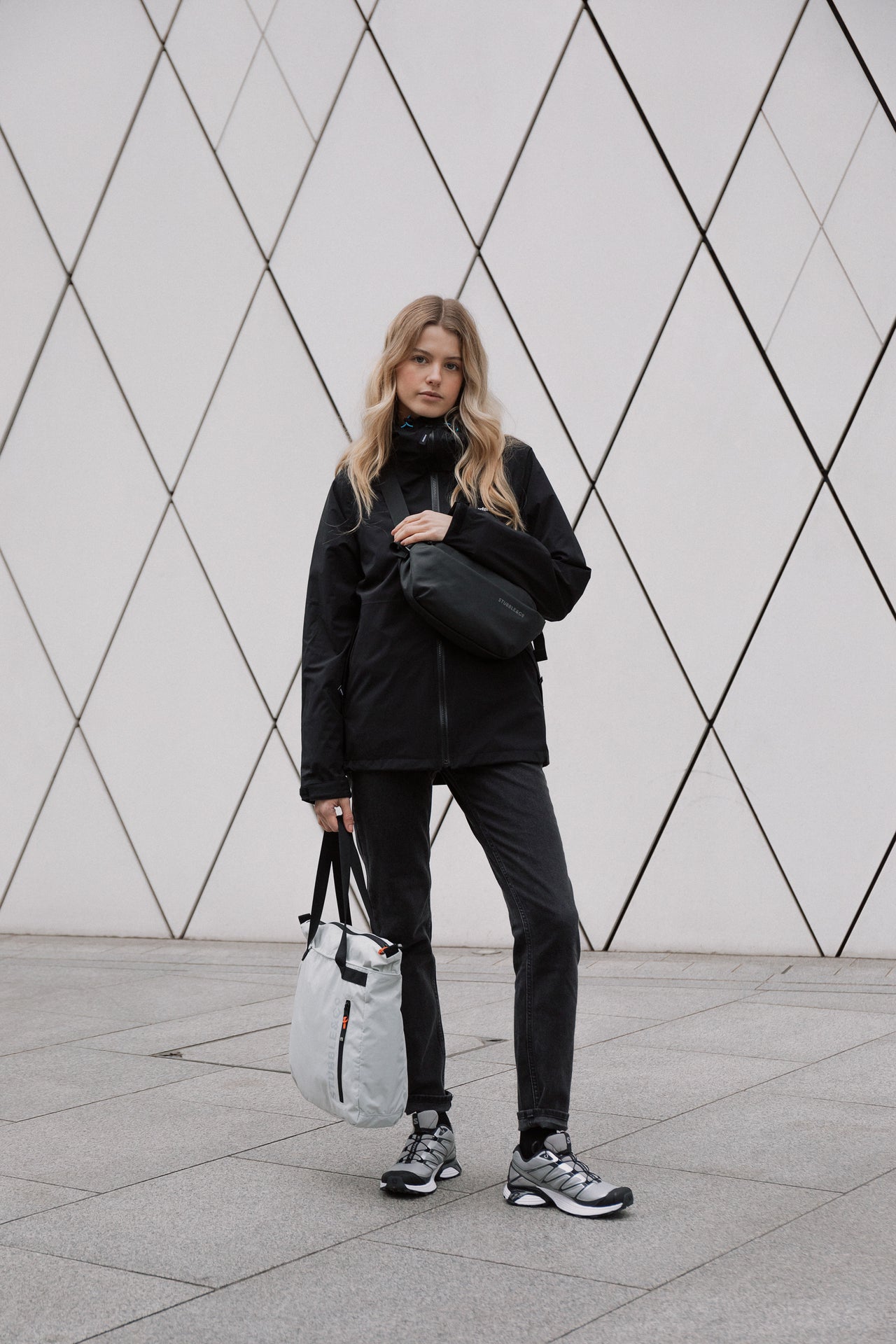 A woman holding an Off White Ultra Light packable bag and wearing a black crossbody bag