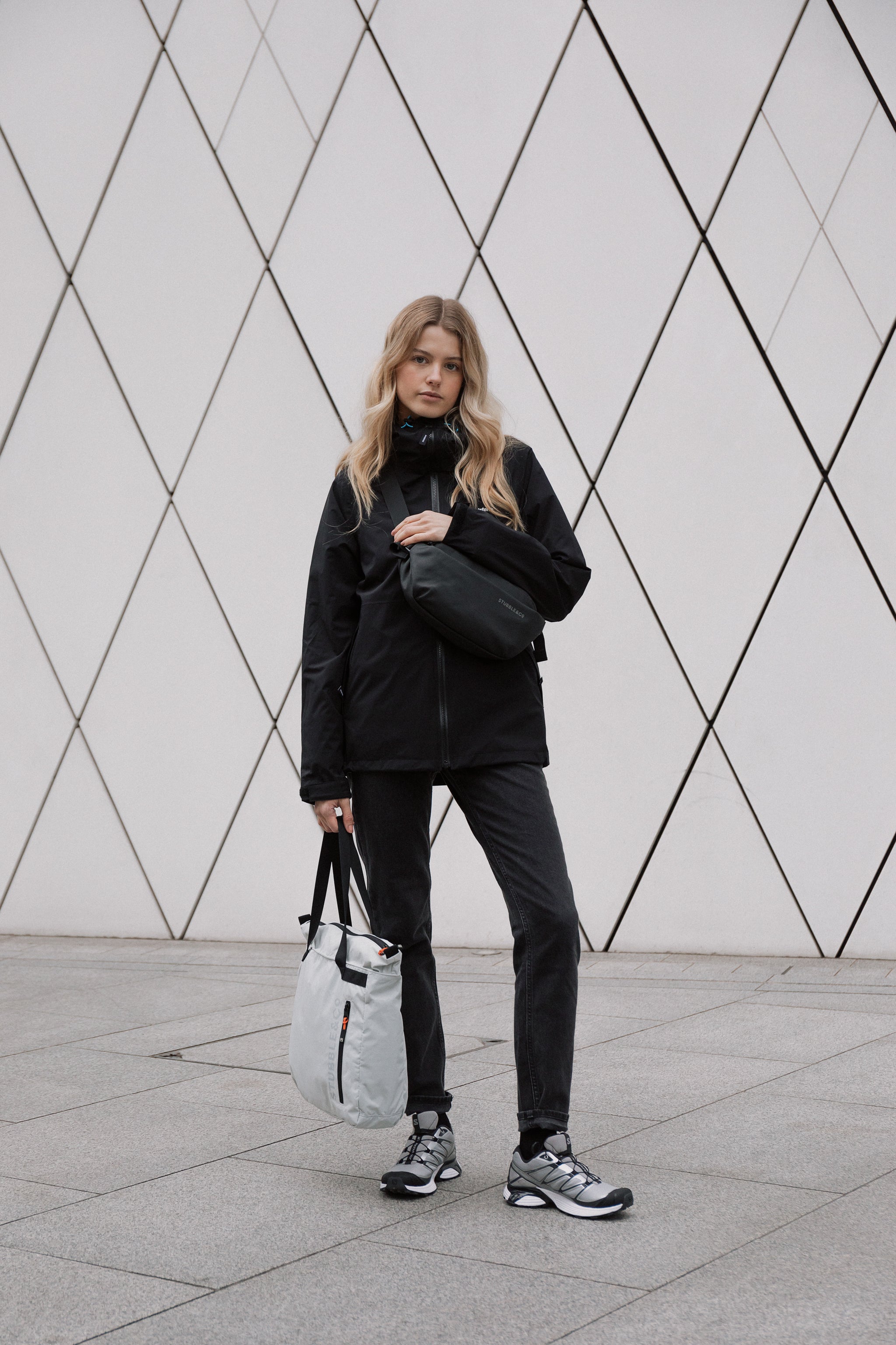 A woman holding an Off White Ultra Light packable bag and wearing a black crossbody bag
