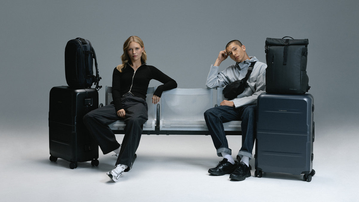 man and women still on airport style bench with collection of suitcases and backpacks