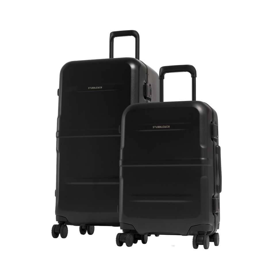 Two hard-shell spinner suitcases in black, one larger and one smaller, standing upright on a clean white studio background. The larger suitcase is behind the smaller one, and both have telescoping handles extended.