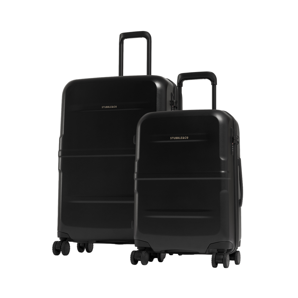 Two black hard-shell spinner suitcases, one larger and one smaller, standing upright on a light gray studio background. The larger suitcase is behind the smaller one, and both have telescoping handles extended.