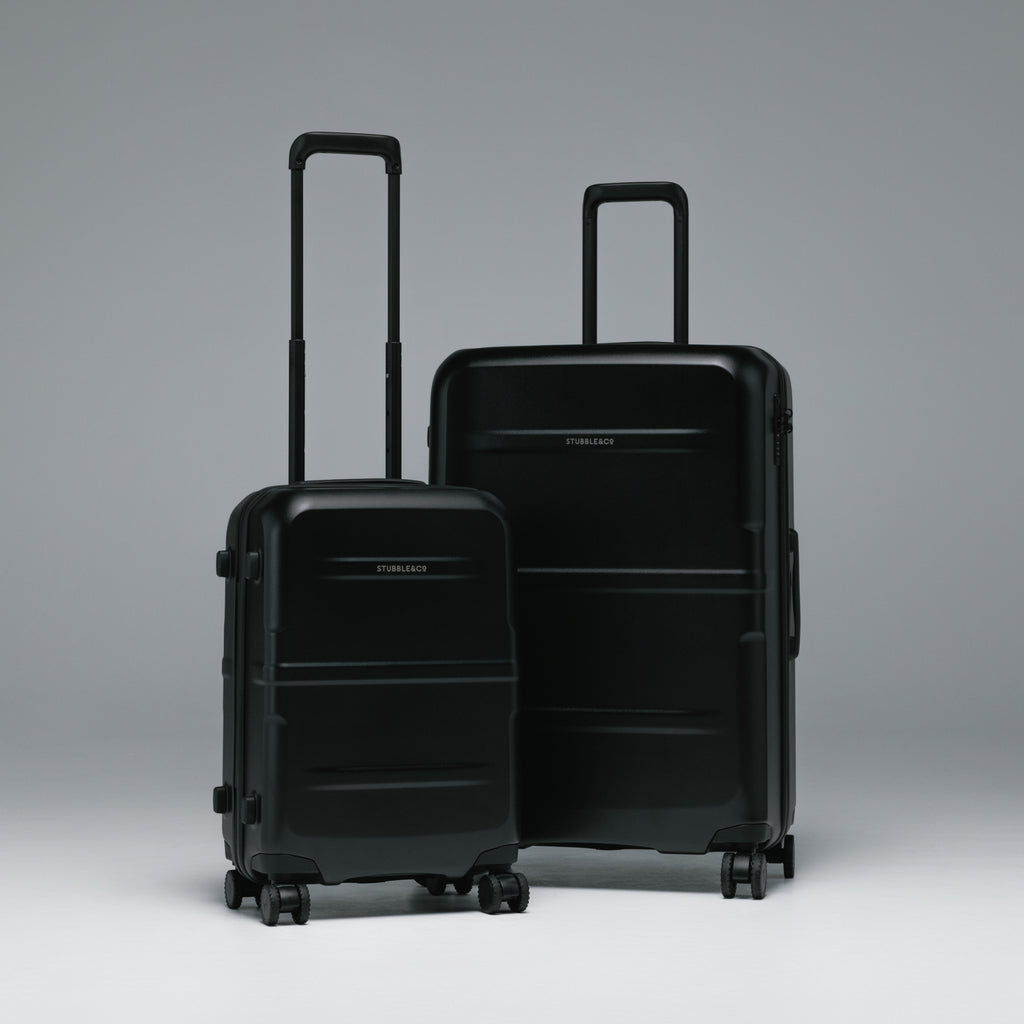 Two black hard-shell spinner suitcases, one smaller and one larger, standing upright with telescoping handles extended against a smooth gray studio background.