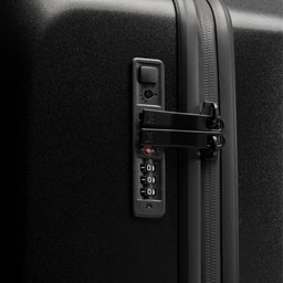 Close-up of a black hard-shell suitcase showing the lock, combination dial, and zipper track. [All variants]
